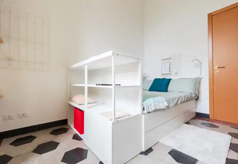 Small, bright bedroom with a built-in platform bed featuring storage drawers and open shelving; soft throw and cushions create a cozy, modern feel.