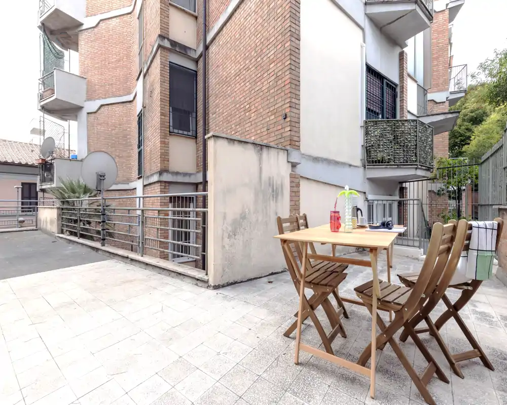 Terraza privada soleada con una pequeña mesa de madera y cuatro sillas plegables — ideal para comidas al aire libre o el café de la mañana. Suelo de baldosas y barandillas ofrecen un espacio exterior de bajo mantenimiento en un entorno urbano.