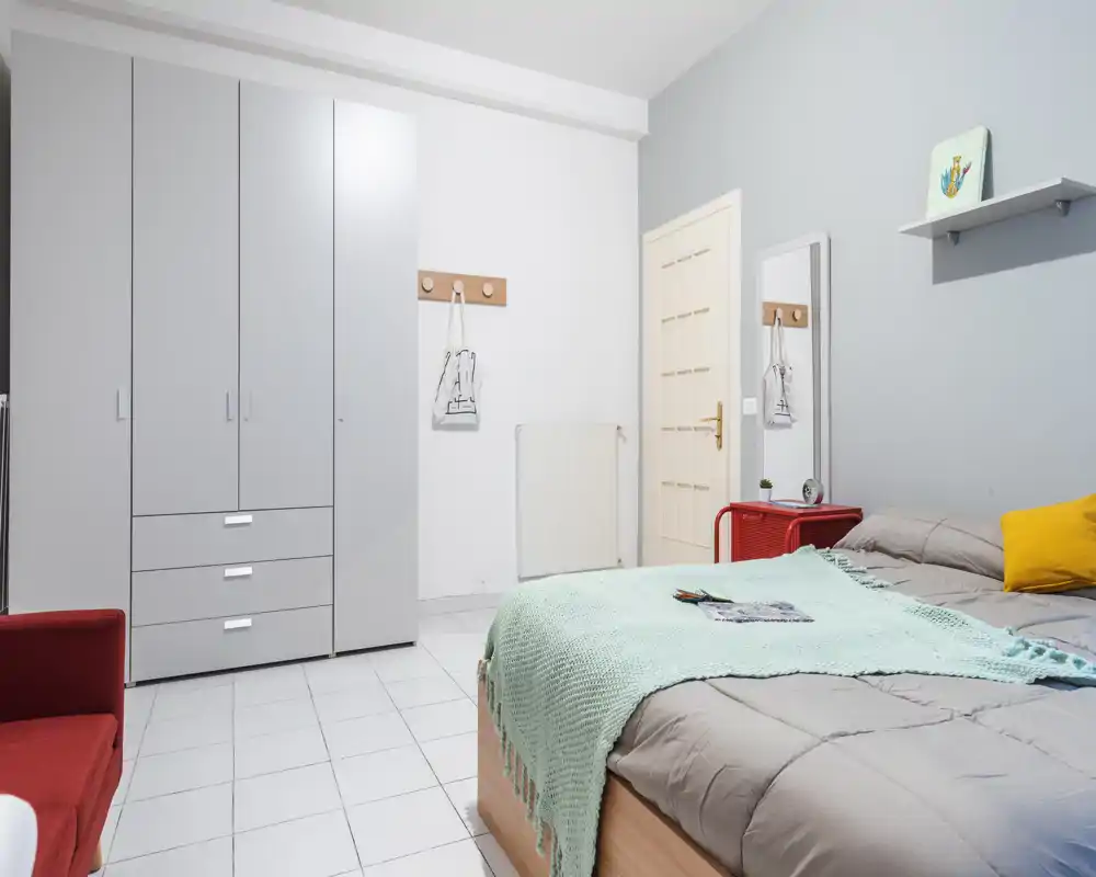 Bright, tidy bedroom with a double bed dressed in neutral linens and a mint throw, a large wardrobe and minimalist decor. The room feels clean and inviting, suitable for listings emphasizing comfort and storage.