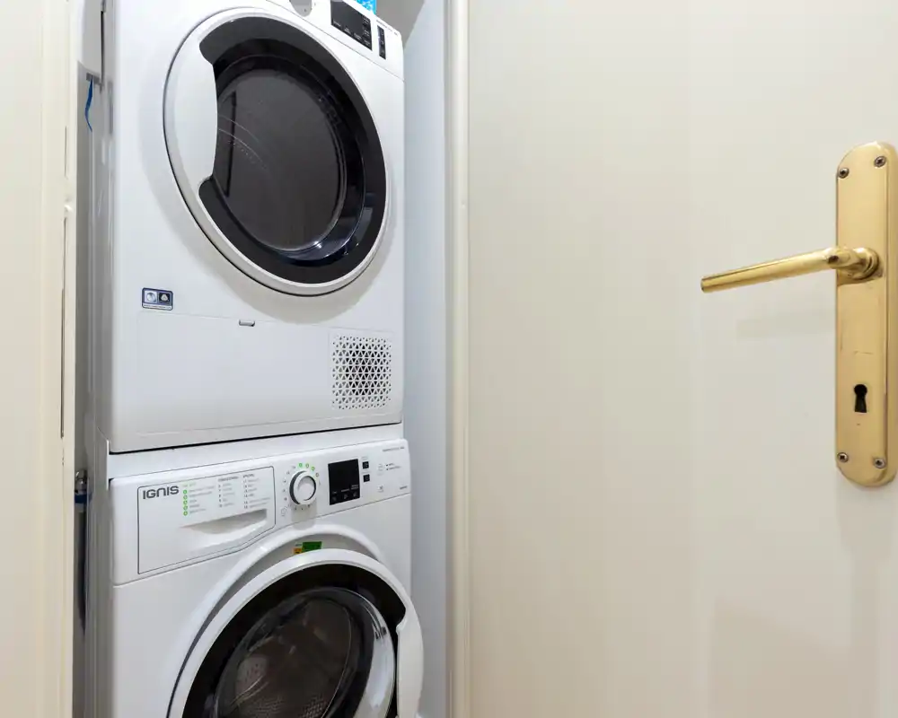 Nicchia lavanderia compatta con lavatrice e asciugatrice sovrapposte accanto a una porta — elettrodomestici moderni e ordinati, ideali per l'uso efficiente dello spazio.