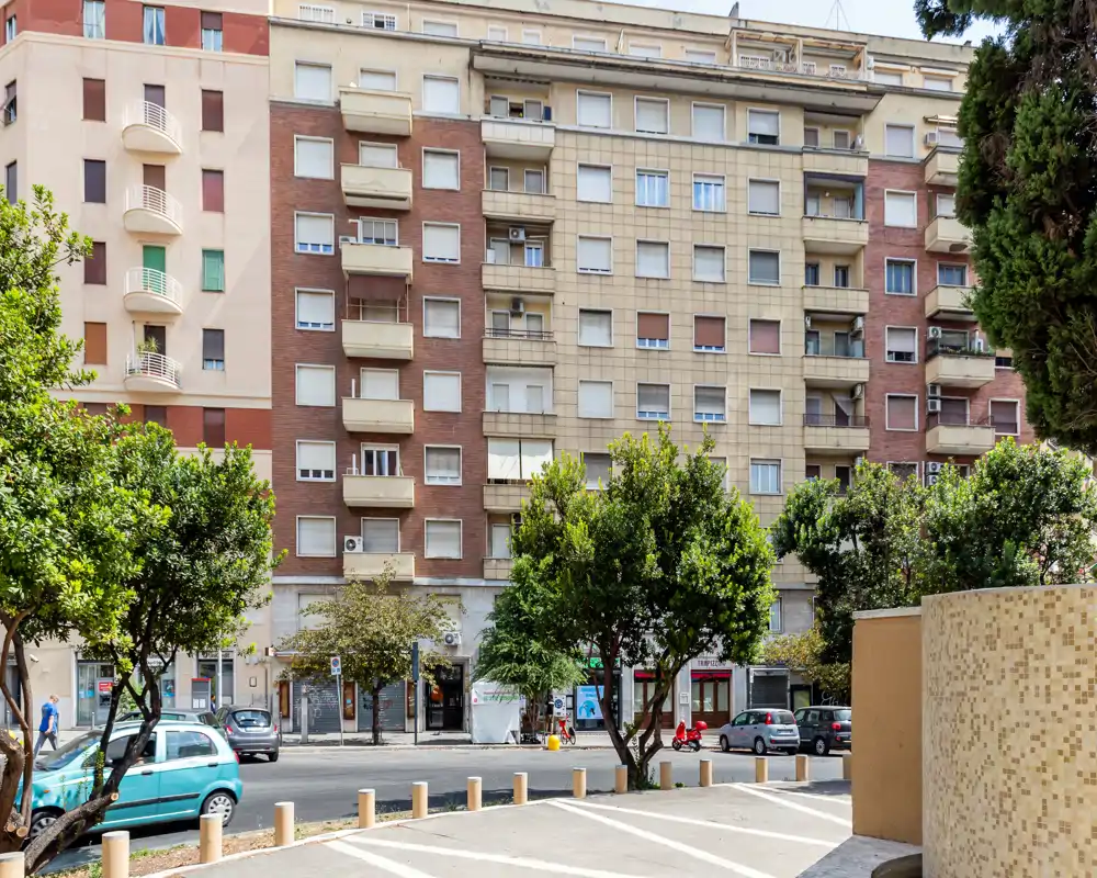 Vista exterior de un edificio residencial con árboles, coches aparcados y aceras a plena luz del día — adecuada para mostrar la fachada urbana o el vecindario.