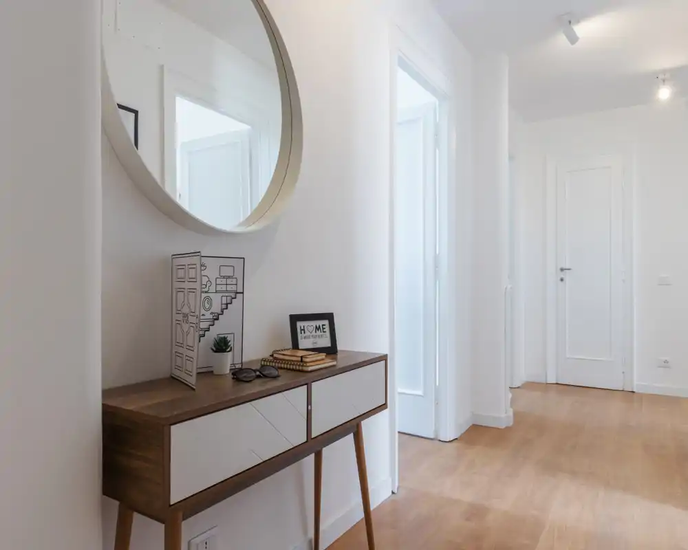 Entrada luminosa y minimalista con consola de madera, espejo redondo y suelo de madera clara — decoración moderna y acogedora.