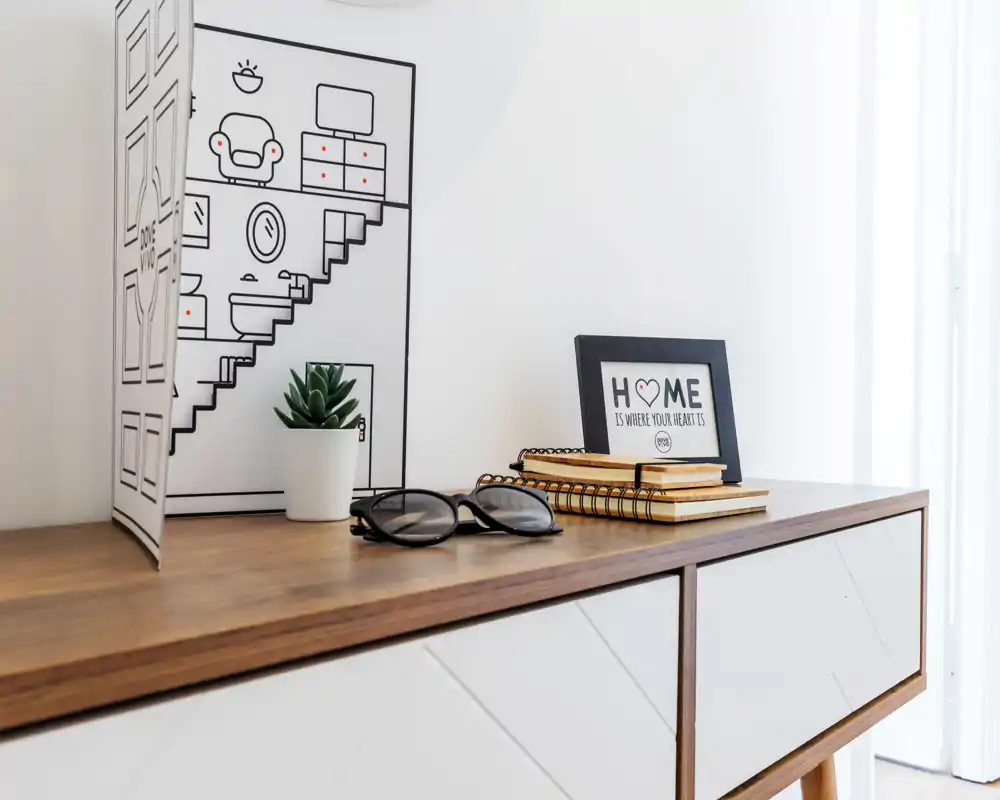 Pequeño rincón luminoso y minimalista en el salón con una consola de madera, marco decorativo, planta y cuadernos.