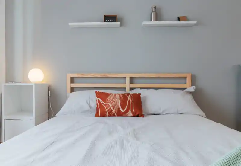 Dormitorio luminoso y minimalista con cabecero de madera, ropa de cama blanca y un cojín decorativo color óxido — estilo limpio ideal para anuncios.