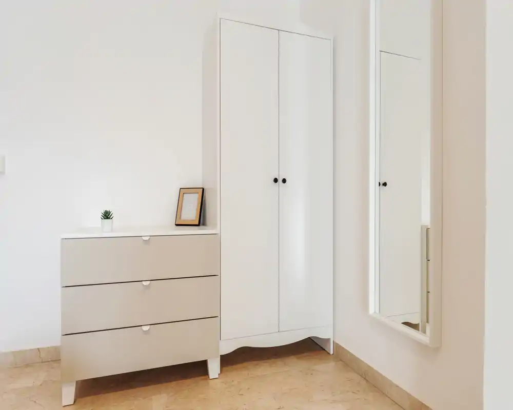Ingresso luminoso e minimale con armadio bianco, comò coordinato e specchio a figura intera a parete, su pavimento chiaro in piastrelle.