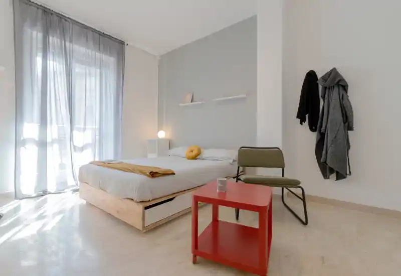 Camera da letto luminosa e minimal con letto basso in legno, biancheria chiara e luce naturale da una finestra ampia; dettagli moderni semplici creano un’atmosfera calma e accogliente.
