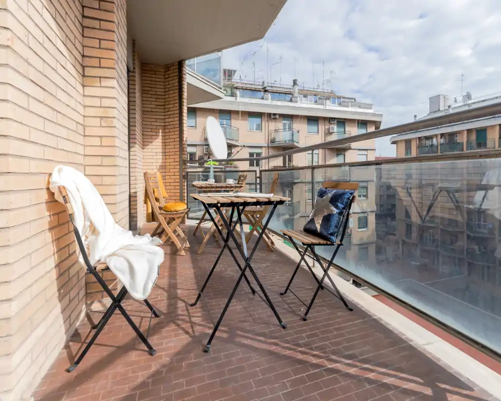 Balcón soleado amueblado con mesa y sillas plegables, barandilla de cristal y vistas a la ciudad — ideal para un café por la mañana o relajarse al aire libre.