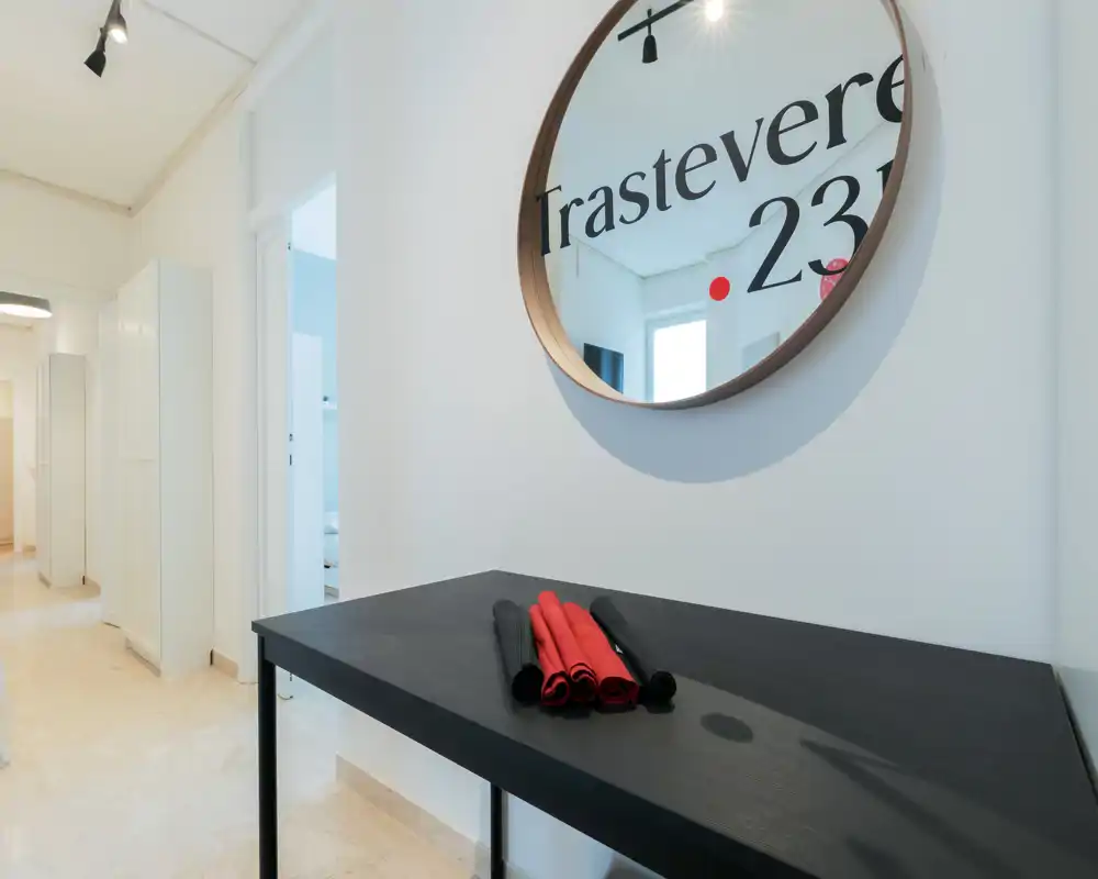 Entrada luminosa y moderna con una consola negra y un espejo redondo en la pared, acentos decorativos mínimos y suelo de piedra claro.