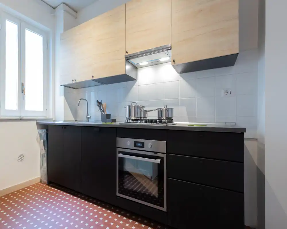 Cocina contemporánea con armarios bajos negros, muebles altos de madera clara, horno empotrado y placa de gas; luz natural y salpicadero de azulejos limpio.