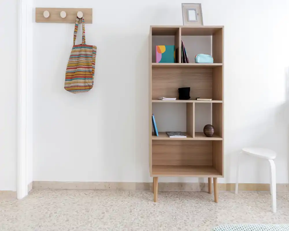 Minimal, well-lit entrance area with a wooden wall hook, a small open shelving unit and a white stool — clean, modern and functional entryway.