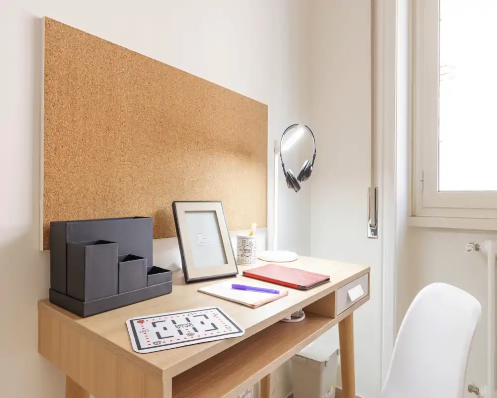 Bright, minimalist workspace with a wooden desk, cork noticeboard, desk lamp and a white chair — ideal for focused study or remote work.