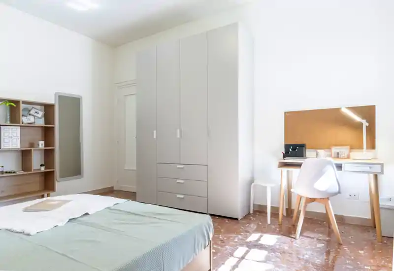 Dormitorio moderno y luminoso con cama visible, armario y un escritorio compacto bañado por luz natural — ideal para estudiantes o alquileres individuales.