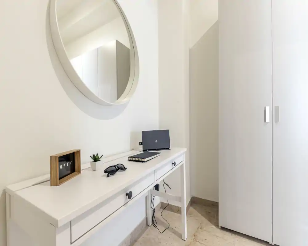 Rincón de entrada luminoso y minimalista con consola blanca, espejo redondo y armario — presentación ordenada para el anuncio.