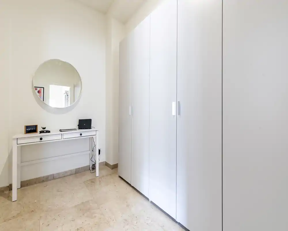 Entrada luminosa y minimalista con un gran armario blanco, una consola estrecha y un espejo redondo: líneas limpias y suelo de piedra pulida que ofrecen una primera impresión cuidada.