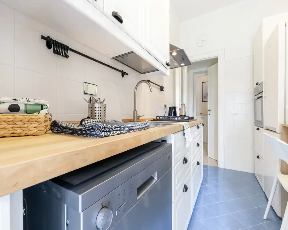 Cocina moderna y luminosa en galería con encimera de madera, electrodomésticos integrados y estilo minimalista, ideal para pisos compactos.