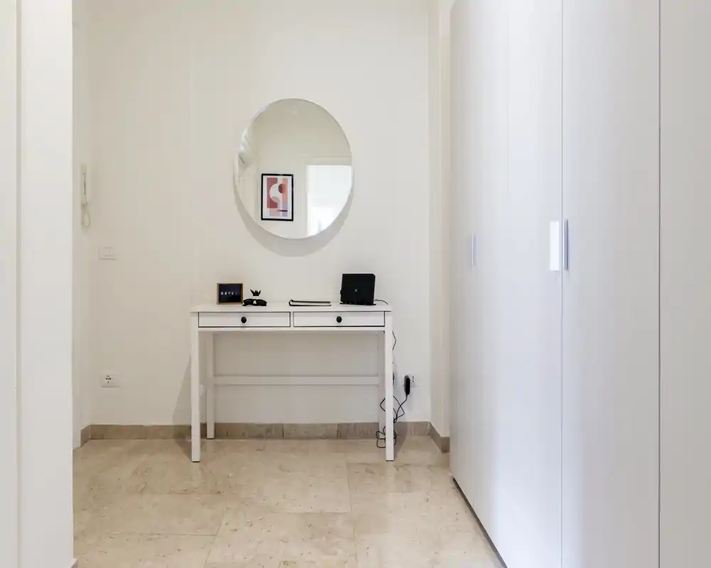 Entrada minimalista y luminosa con consola estrecha, espejo redondo y armario empotrado — recibidor limpio y moderno ideal para anuncios.