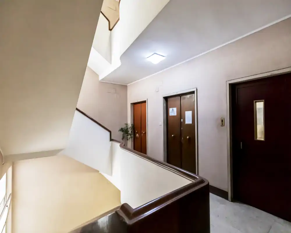 Escalera/vestíbulo comunitario con puertas de pasillo y acceso a ascensor; iluminación neutra y líneas limpias, ideal para mostrar la entrada del edificio.