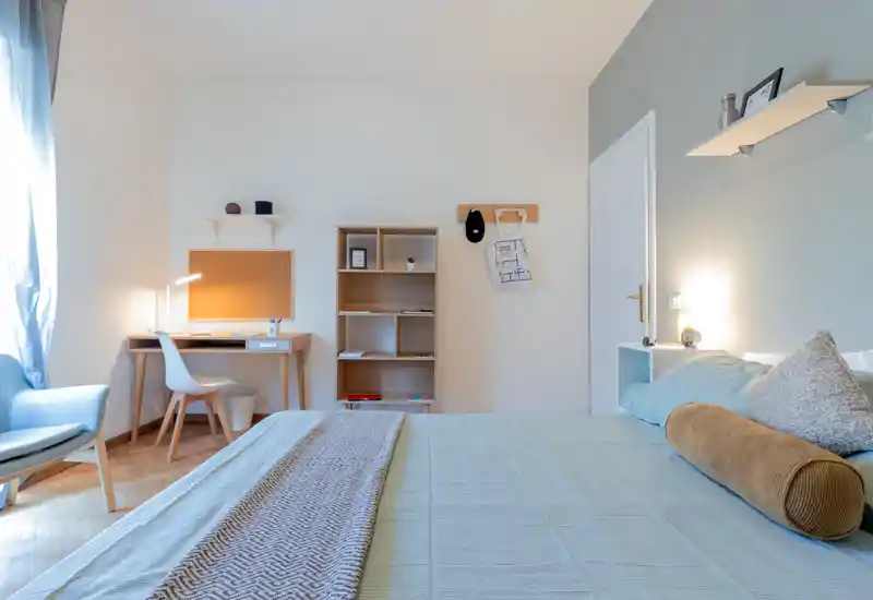 Bright, well-staged bedroom with a large bed in the foreground, soft textiles, a reading chair by the window and a small desk — ideal for comfortable stays.