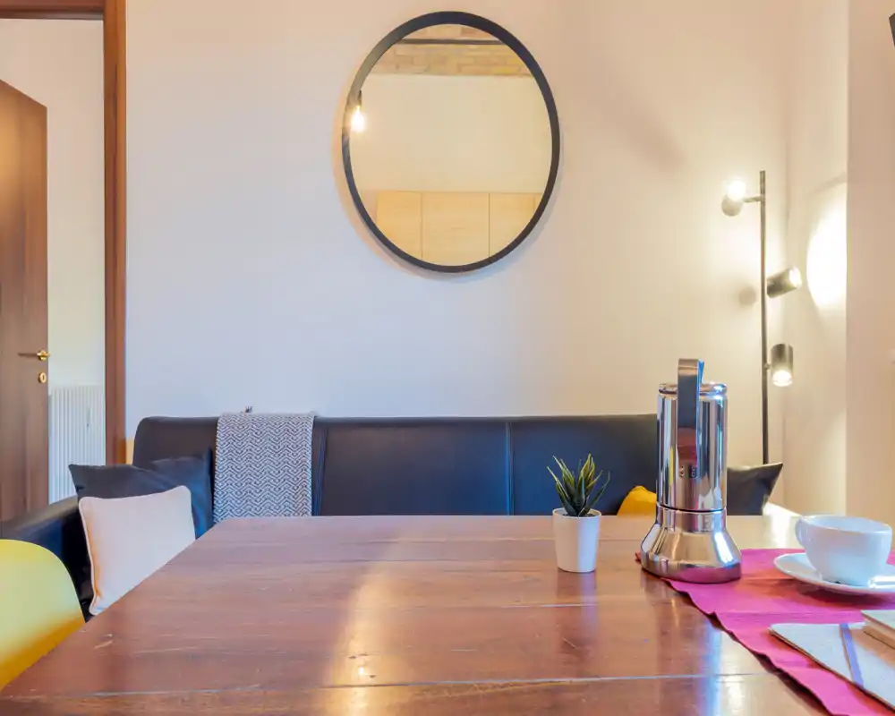 Acogedor rincón comedor con mesa de madera, banco sofa y luz cálida — ideal para comidas relajadas.