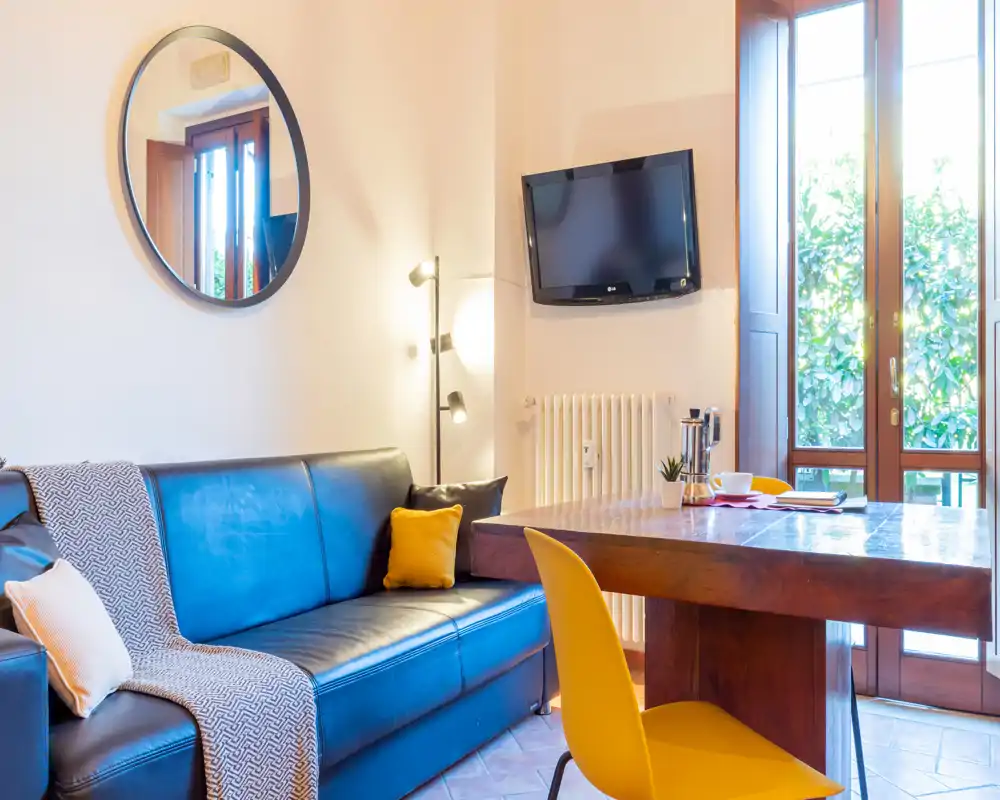 Sala de estar luminosa y moderna con sofá de cuero, sillas amarillas de acento y una mesa de madera junto a grandes puertas de cristal que aportan mucha luz natural.