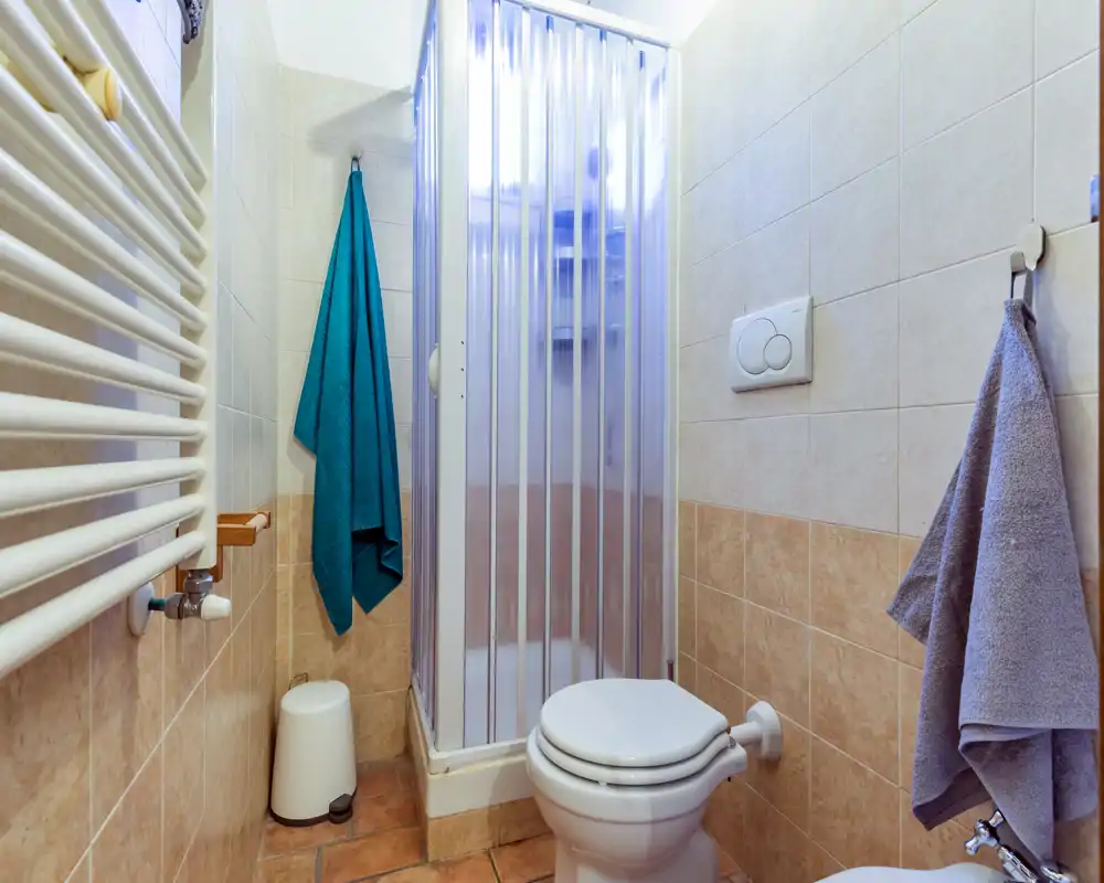 Baño compacto y bien iluminado con mampara de ducha, inodoro, toallero y paredes alicatadas — ideal para un apartamento pequeño o baño de invitados.