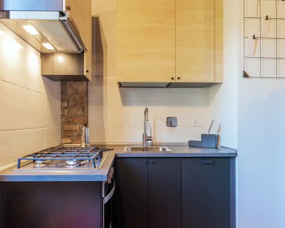 Cuisine moderne et compacte avec plaque à gaz, évier inox et placards en bois clair — lumineuse et bien agencée, parfaite pour un appartement citadin.