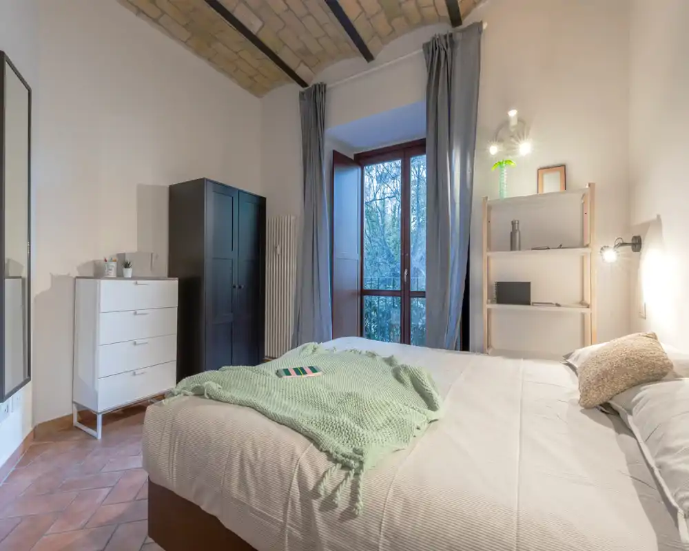 Camera da letto doppia luminosa e ben arredata con soffitto a volta in mattoni, ampia finestra, armadio e morbidi tessuti che la rendono accogliente.