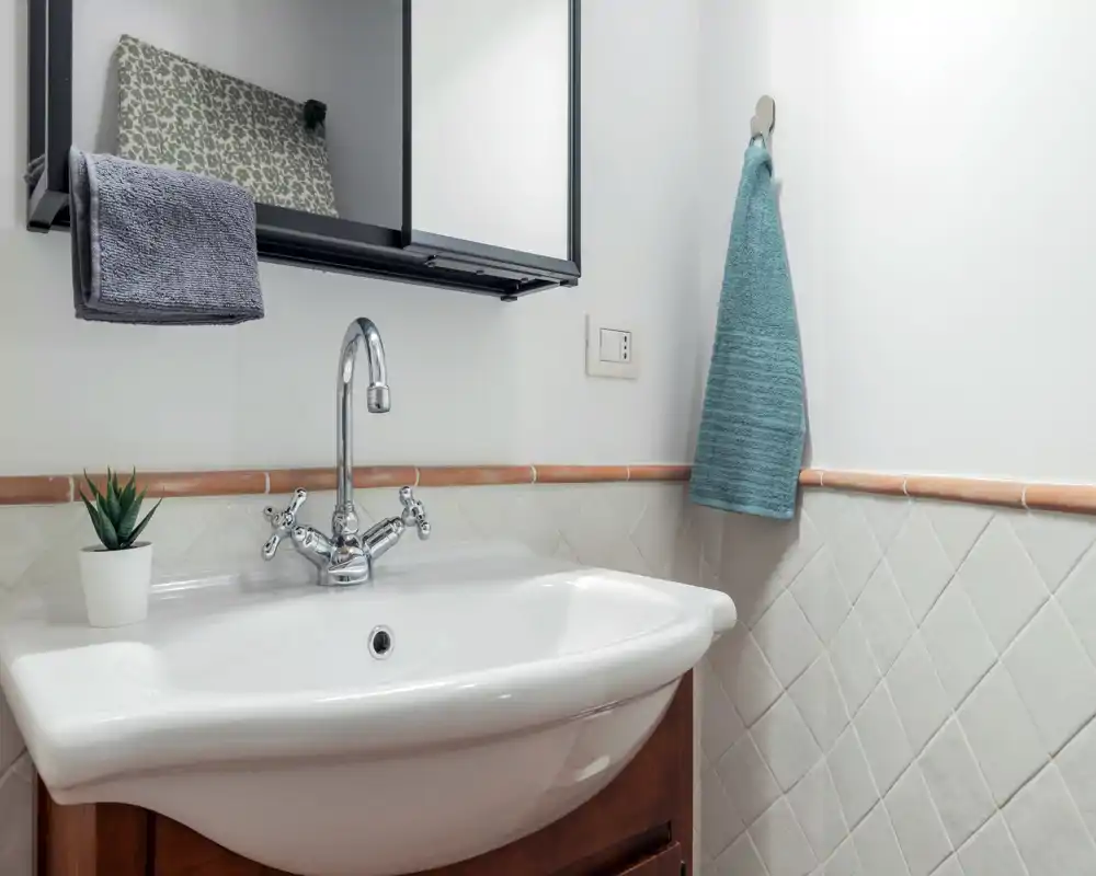 Lavabo da bagno luminoso e pulito con miscelatore cromato classico, piastrelle a mezza parete e un asciugamano appeso — perfetto per mostrare un bagno per gli ospiti.
