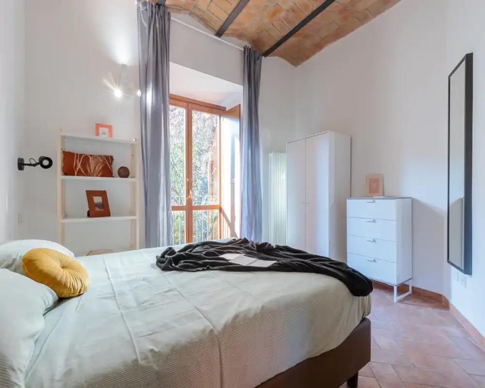 Chambre lumineuse et accueillante avec un grand lit, textiles doux et lumière naturelle provenant d'une grande fenêtre ; plafond en briques cintré apportant du caractère.