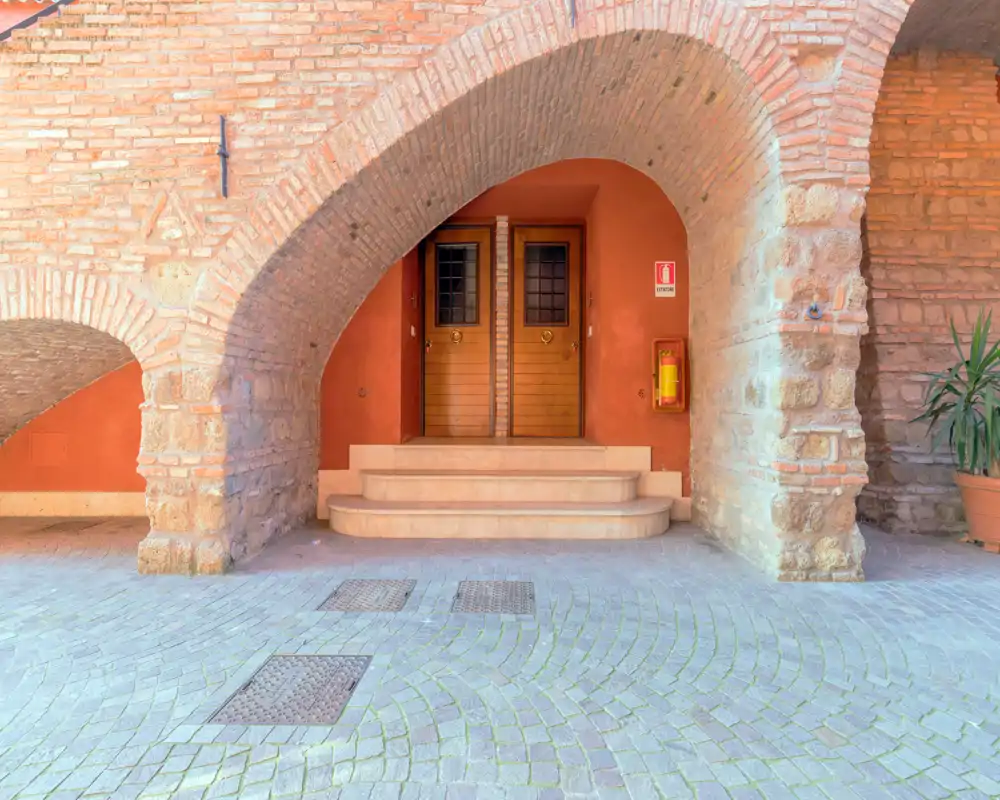 Charmante entrée extérieure en arcade avec portes en bois jumelles, colonnes de pierre et briques chaleureuses — idéale pour présenter un passage extérieur historique.