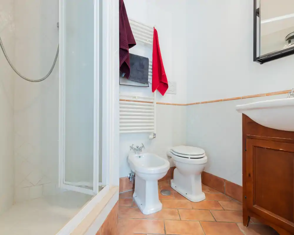 Baño limpio y luminoso con ducha, bidé, inodoro y mueble con lavabo. Suelo de terracota y azulejos blancos en las paredes ofrecen un aspecto cálido y clásico.