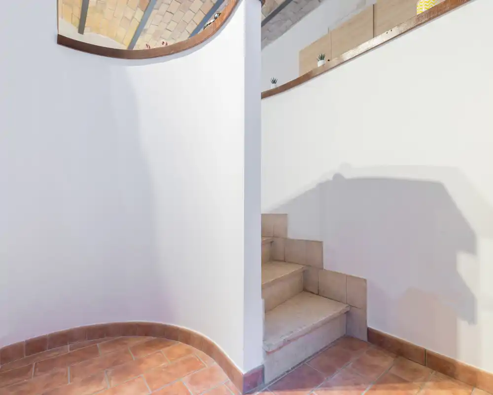 Entrada luminosa con suelo de baldosas, una pequeña escalera interior y paredes blancas curvas que definen la transición entre niveles.