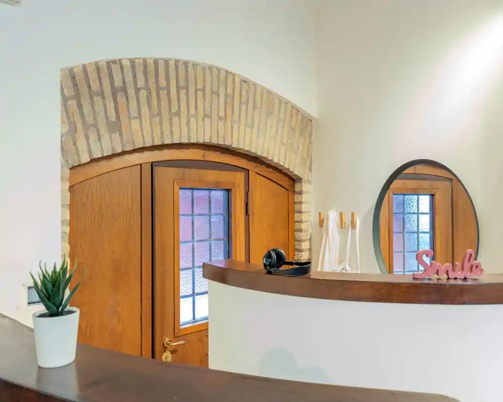 Entrada luminosa y cuidada con puerta de madera en un arco de ladrillo, cristales decorativos y un pequeño mostrador: primera impresión acogedora.