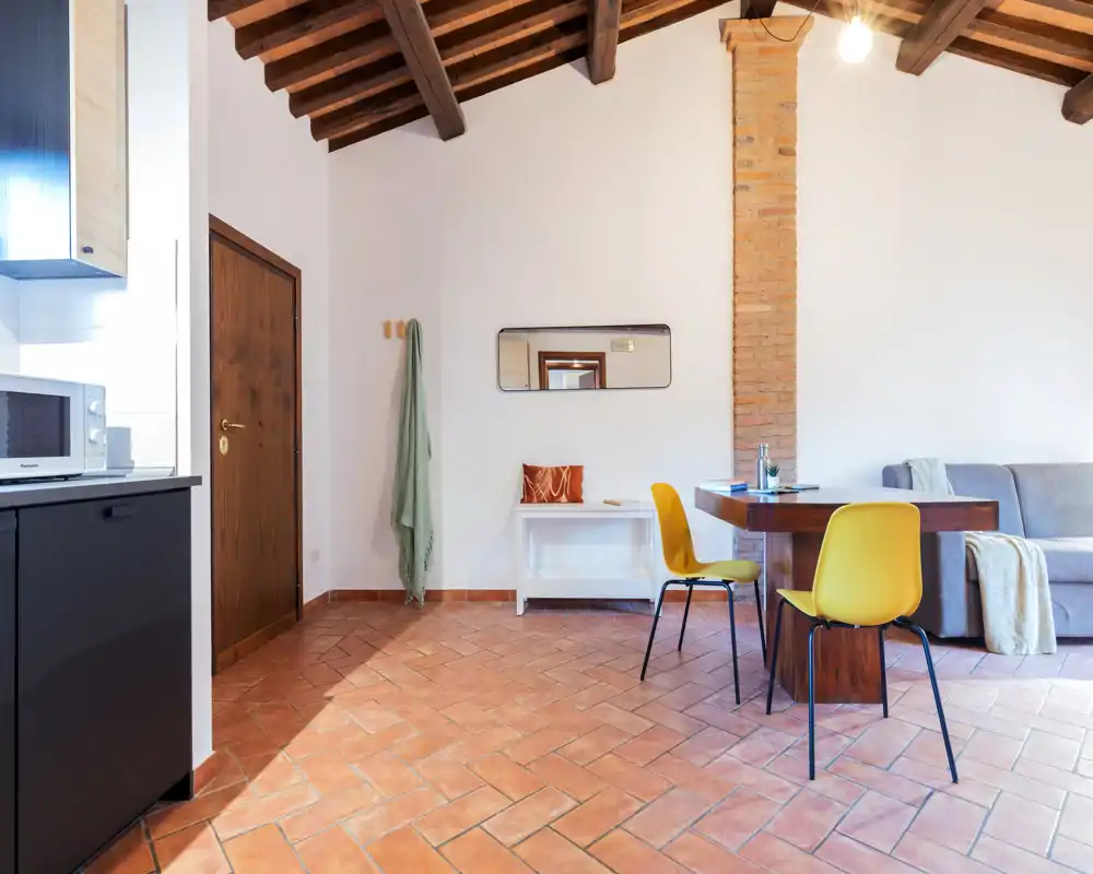 Zona de estar luminosa y con estilo, con vigas de madera a la vista, suelo de terracota, mesa de comedor compacta y un sofá cómodo — ideal para una estancia acogedora.