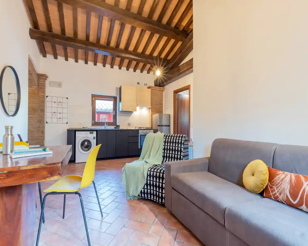 Bright, stylish living area with exposed wooden beams, a comfortable sofa and an integrated kitchenette — ideal for a cozy city stay.