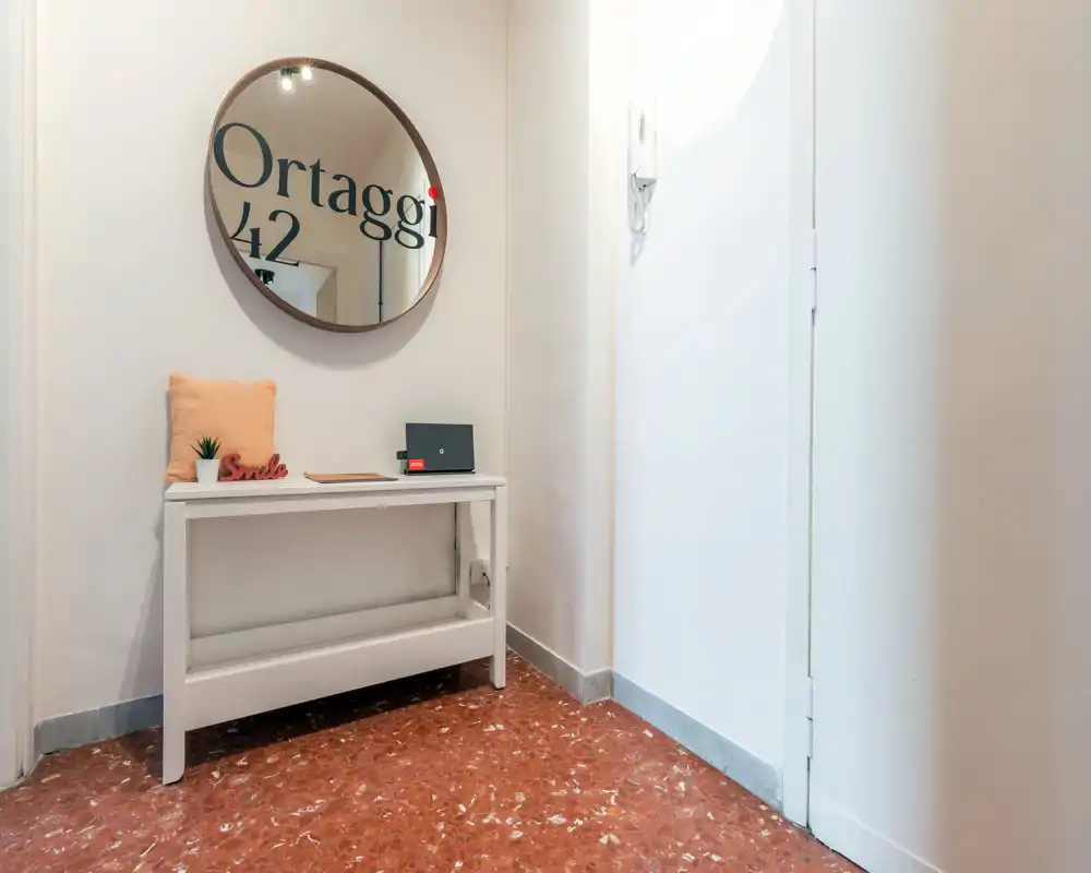 Ingresso luminoso e ordinato con un piccolo tavolino consolle, cuscino decorativo e specchio rotondo — un’accogliente area d’ingresso perfetta per accogliere gli ospiti.
