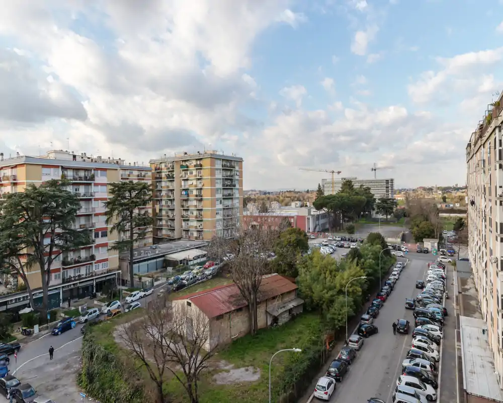Ampia vista urbana da un piano alto con condomini, auto parcheggiate, alberi e cielo parzialmente nuvoloso — ideale per mostrare il quartiere e il contesto stradale.