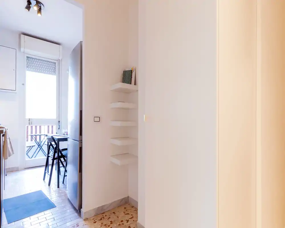 Cucina compatta e luminosa con piccolo tavolo da pranzo, frigorifero e porta sul balcone — perfetta per un appartamento in città.