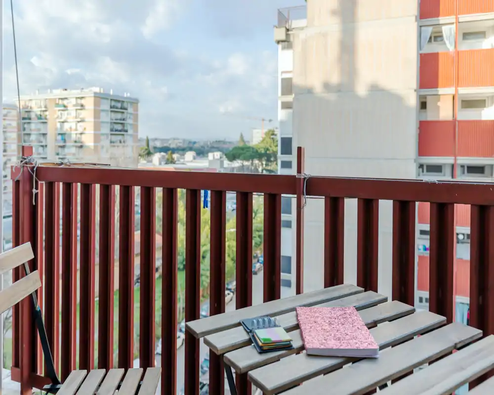 Piccolo balcone urbano con tavolino bistro in legno e sedia pieghevole, con vista sugli edifici circostanti — luce diurna luminosa e angolo esterno compatto ideale per un caffè mattutino.