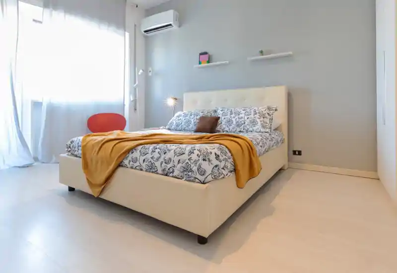 Camera da letto luminosa e ben arredata con un ampio letto imbottito, biancheria con motivo e un caldo plaid. La luce naturale riempie la stanza, creando un’atmosfera calma e accogliente, perfetta per annunci.