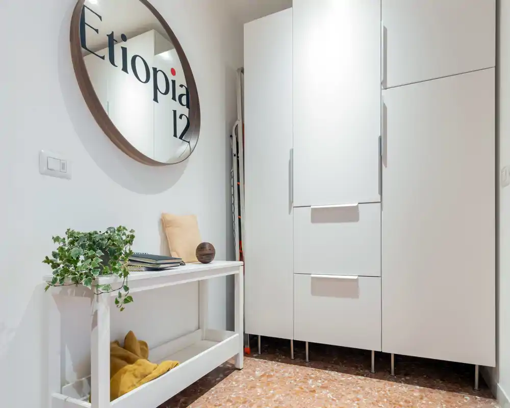 Bright, minimal entrance with a white console table, round wall mirror and built-in storage cupboards—stylish and welcoming hallway corner.