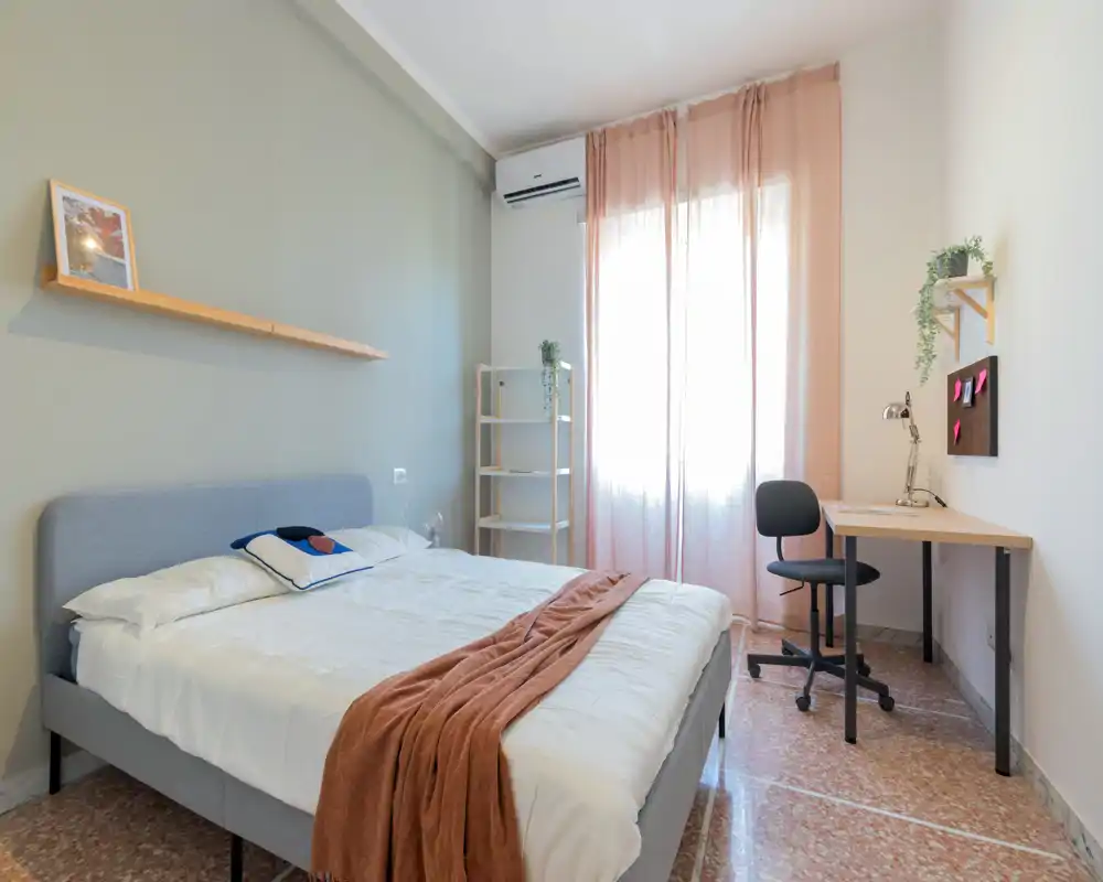 Camera da letto luminosa e ben arredata con letto matrimoniale, tessili accoglienti e una piccola postazione vicino alla finestra — perfetta per un soggiorno confortevole.