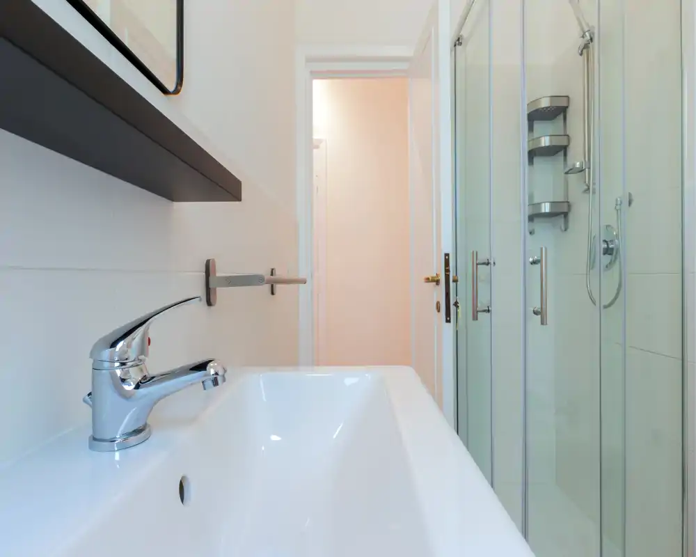 Bagno moderno e luminoso con lavabo bianco e doccia con pareti in vetro; rubinetteria cromata e piastrelle pulite per un aspetto minimale e fresco.