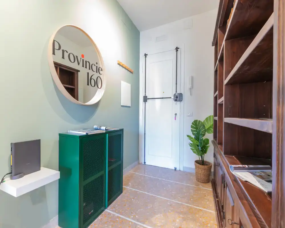 Ingresso luminoso e ordinato con uno specchio rotondo decorativo, mobile verde per riporre e una scaffalatura in legno accanto alla porta — ottima prima impressione.