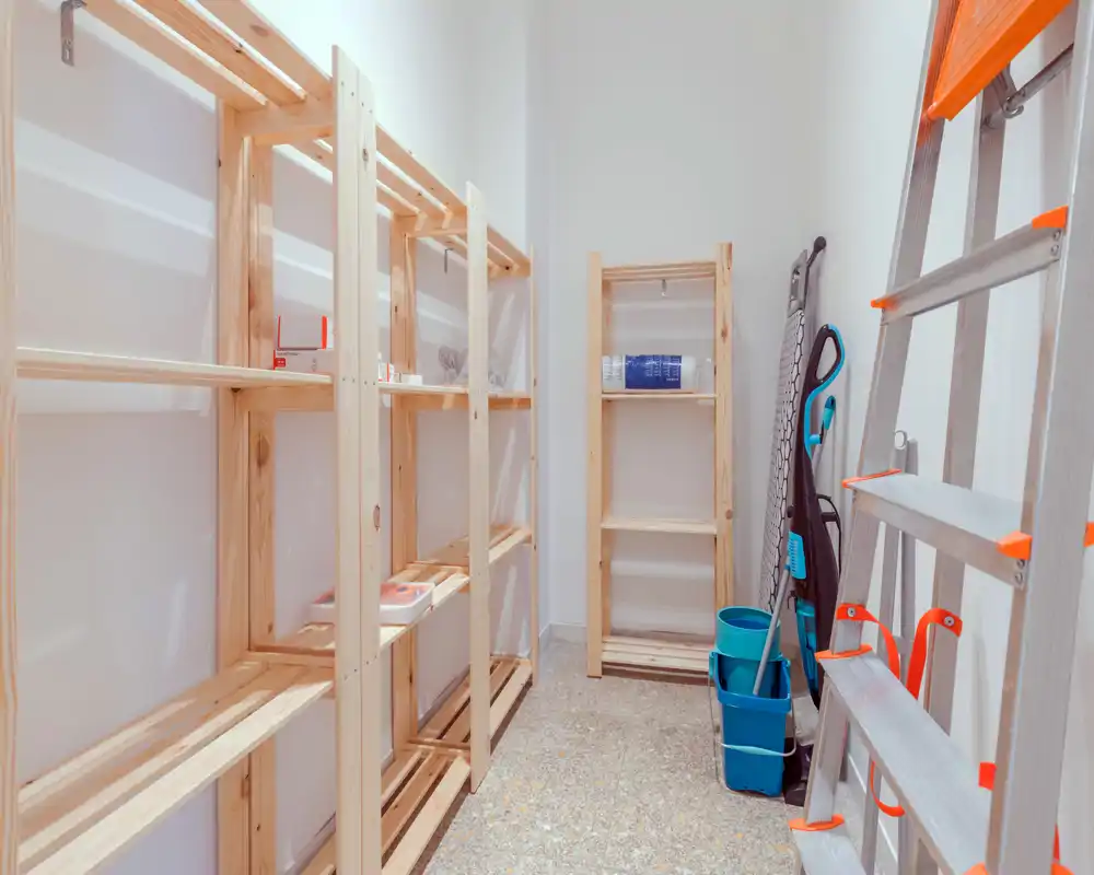 Piccolo ripostiglio/locale di servizio con scaffalature in legno, scala e attrezzi per la pulizia — ordinato e pronto per essere organizzato.