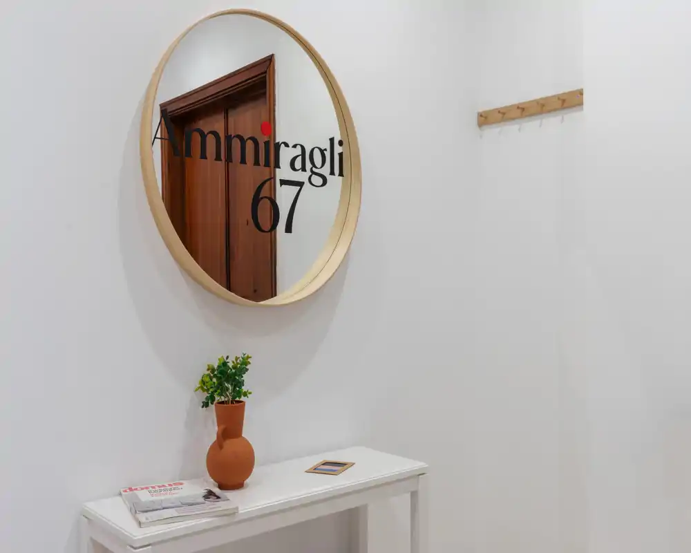 Entrée lumineuse et minimaliste avec un miroir rond, une petite console, un vase décoratif et des patères murales — un espace d'accueil soigné et accueillant.