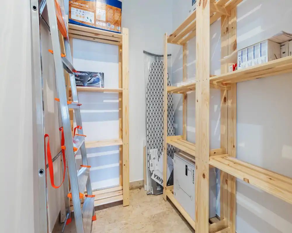 Petit local de rangement/utility avec étagères en bois, échelle et cartons — idéal pour organiser outils ou fournitures ménagères.