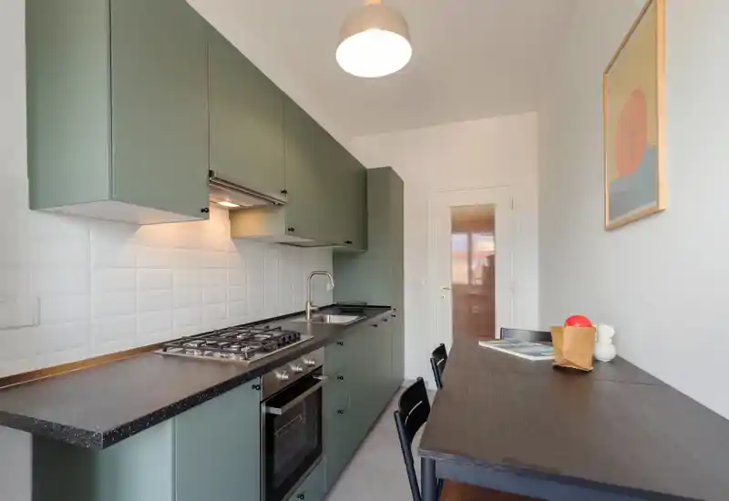 Cuisine en longueur moderne avec meubles verts mats, plaque à gaz, four encastré et petit comptoir repas — lumineuse, bien agencée et prête à l'emploi.