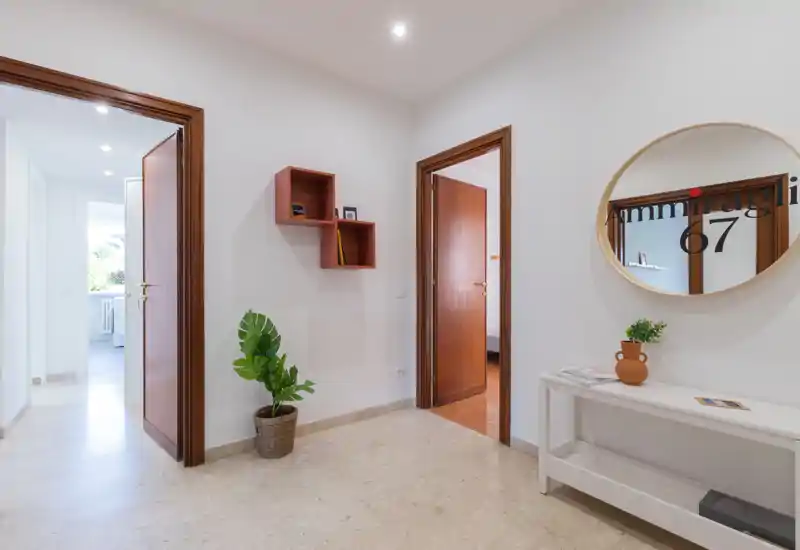 Entrée lumineuse et accueillante avec console blanche, miroir rond et plante décorative. Sol en marbre et encadrements de porte en bois apportent une première impression neutre et agréable.