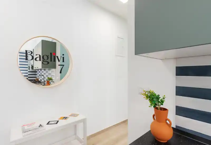 Entrée lumineuse et minimaliste avec un miroir rond reflétant une partie de l'intérieur, un petit banc blanc pour clés et magazines et un vase en terre cuite décoratif sur le plan de travail.